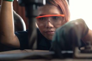 Diverse female certified industrial engineer operating factory drill machinery - Engineering student concentrating on production drilling for manufacturing business - Training and learning concept